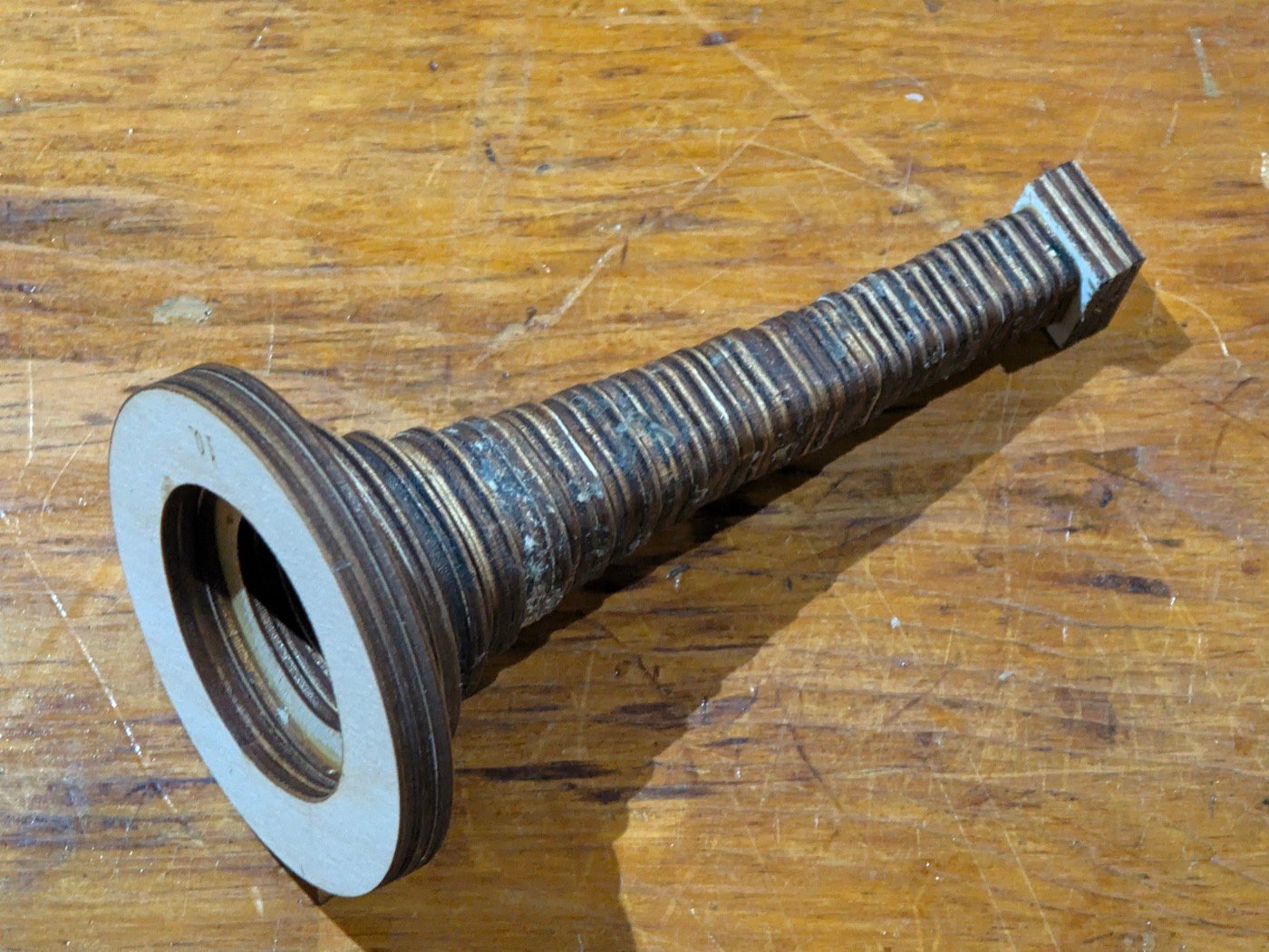 The bell as built, lying on a workbench: laminated ply rings stacked from a small square block at the throat, widening and rounding as they climb to a flat round rim