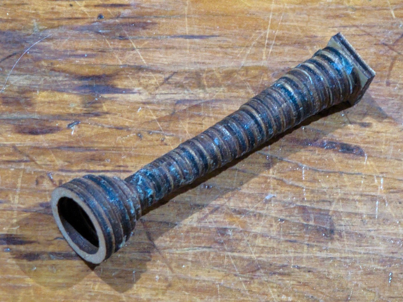 The mouthpiece as built, lying on a workbench: a square block at one end, a ring-stacked shaft narrowing to a waist, and a small cup at the other end