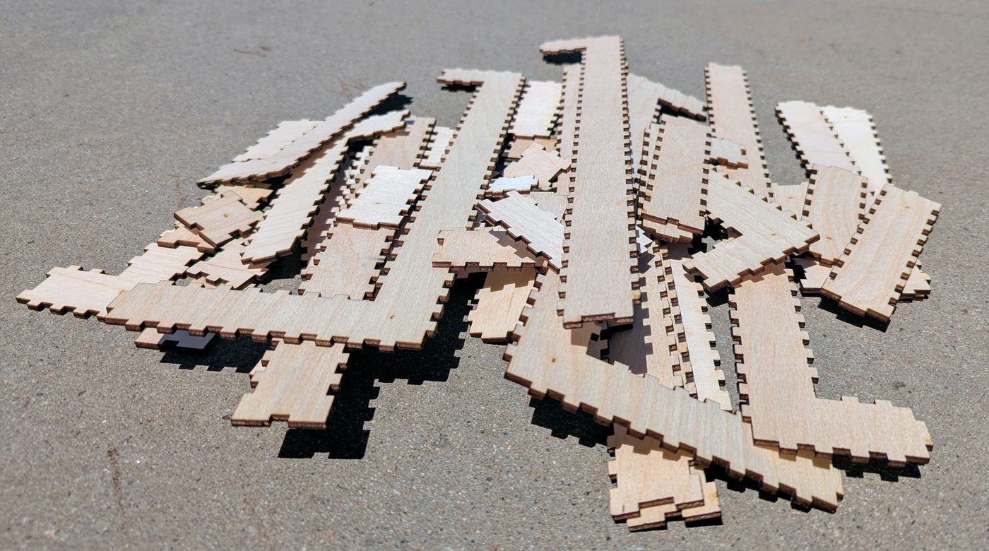 A pile of finger-jointed birch plates on the ground, cut and not yet glued, their teeth and notches visible along every edge